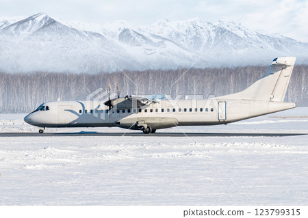 White passenger turboprop aircraft taxiing at the main taxiway at a winter airport on the background of high snow capped mountains 123799315