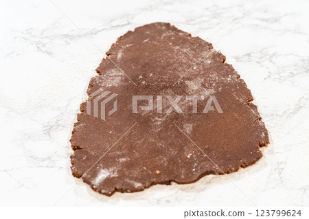 Overhead view of chocolate cookie dough partially rolled out on a floured marble surface, prepped for cookie cutting. Overhead view of chocolate cookie dough partially rolled out on a floured marble surface, prepped for cookie cutting. 123799624