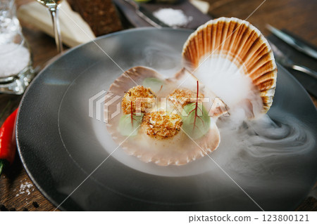 Grilled scallops served in a shell with avocado mousse and microgreens. Elegant seafood dish presented with dry ice smoke. Gourmet cuisine in a fine dining restaurant 123800121