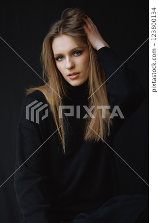 Relaxed portrait of a woman adjusting her hair, dressed in a black sweater. The candid moment, natural lighting, and warm tones add a contemporary, effortless, and stylish touch Relaxed portrait of a woman adjusting her hair, dressed in a black sweater. The candid moment, natural lighting, and warm tones add a contemporary, effortless, and stylish touch 123800134