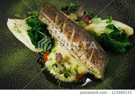 An artfully plated fish dish garnished with fresh greens and sauce, offering a delicious experience 123800135