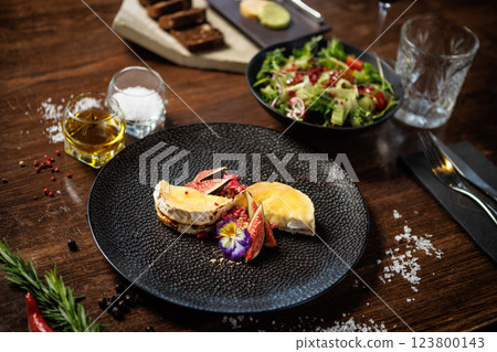 Gourmet cheese plate with figs and edible flowers. Fresh salad with tomatoes and greens. Fine dining experience in a modern restaurant. Healthy and delicious meal closeup 123800143