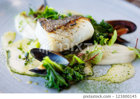 Cod fillet with cauliflower cream, asparagus, clam-wine sauce and mussles. Delicious seafood fish closeup served on a table for lunch in modern cuisine gourmet restaurant Cod fillet with cauliflower cream, asparagus, clam-wine sauce and mussles. Delicious seafood fish closeup served on a table for lunch in modern cuisine gourmet restaurant 123800145