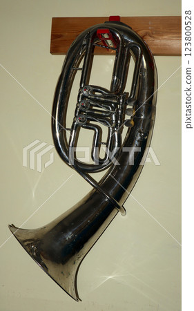 Baritone brass wind musical instrument elegantly displayed on hanger against a wall Baritone brass wind musical instrument elegantly displayed on hanger against a wall 123800528