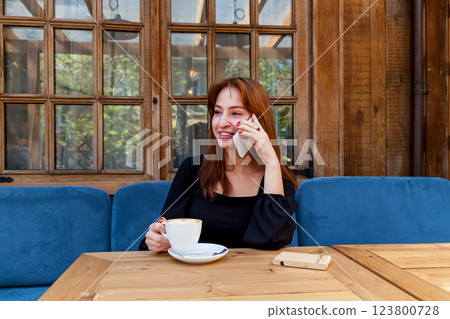 A girl in a cafe at a table talking on the phone 123800728