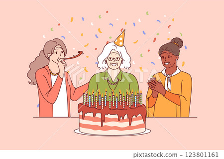 Birthday of elderly woman standing near large cake with candles and happy friends 123801161