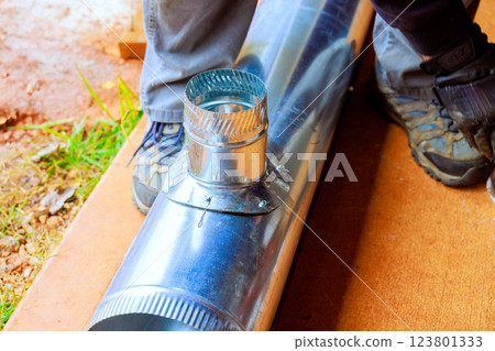 Worker attaches circular metal HVAC fitting to ventilation pipe while kneeling on construction site 123801333