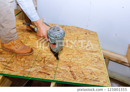 Contractor is utilizing nail gun to secure oriented strand board in works on assembly process. Contractor is utilizing nail gun to secure oriented strand board in works on assembly process. 123801355