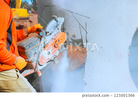 Construction worker operates concrete cutting saw, creating dust during build works area at construction site 123801366