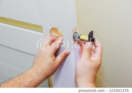 Hands installing lock cylinder into door at home during renovation Hands installing lock cylinder into door at home during renovation 123801376