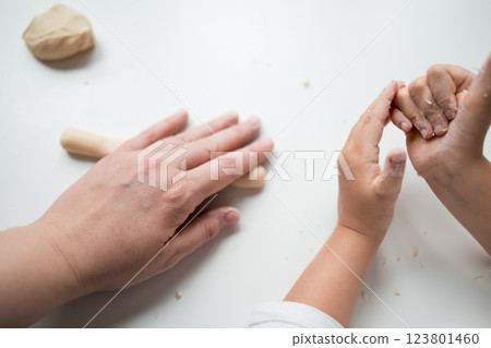 Caucasian adult and child hands working with dough on white surface 123801460