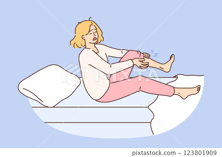 Night cramp woke up woman clutching leg and in pain, sitting in bed with blanket and pillow 123801909