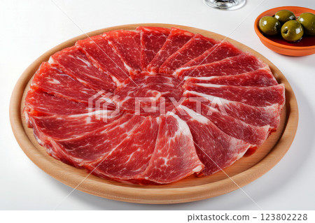 Thinly sliced Jamon Iberico with rich fat marbling, served with olives and crusty bread, showcasing its glossy texture and savory flavor, traditional Spanish dish 123802228