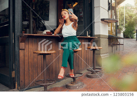 Restaurant, woman and influencer taking a phone selfie for social media content for online followers outdoors. Lifestyle, cafe and young person blowing a kiss on a photo enjoying summer holidays 123803156