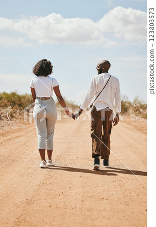 Black couple, love and holding hands back view in nature walking on vacation on desert, sand or dirt road. Romance, safari and man, woman and bonding, care or spending time together on outdoors date. Black couple, love and holding hands back view in nature walking on vacation on desert, sand or dirt road. Romance, safari and man, woman and bonding, care or spending time together on outdoors date. 123803573