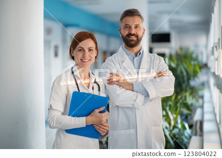 Portrait of two doctors in hospital hallway, holding medical records in hand. 123804022