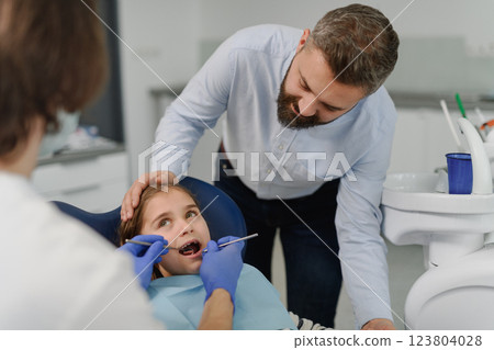 Girl during annual dental check-up in dental clinic, father supporting her. 123804028