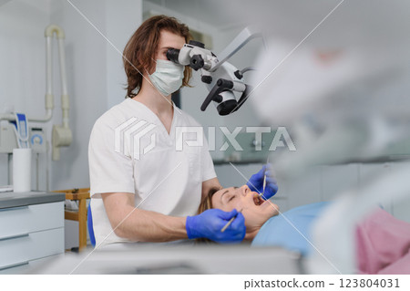 Male dentist doing dental procedure in dental clinic, using dental microscope. 123804031