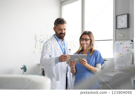Dentist and female nurse looking at appointment schedule in tablet. Healthcare workers in Doctor's Office. 123804098
