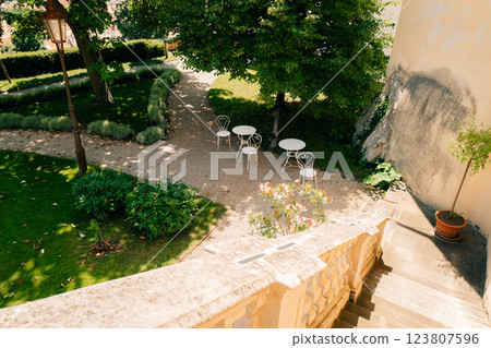 Peaceful garden terrace with chairs, tables, greenery, and colorful flowers 123807596
