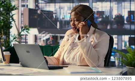 Black business director on a phone call discusses key business tasks, focusing on decision making and budget planning. Manager multitasking business operations and task management. Camera A. 123807895