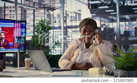 Chief executive officer calling her secretary on office landline phone, asking about important paperwork to solve business tasks for development. African american boss does task management. Camera B. Chief executive officer calling her secretary on office landline phone, asking about important paperwork to solve business tasks for development. African american boss does task management. Camera B. 123807985