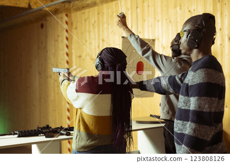 Shooting gallery staff member teaching student how to hold and handle pistol. Firing range specialist providing guide to woman learning how to achieve high level of proficiency with firearms 123808126