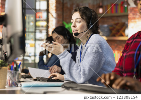 Call center operator next to coworkers dealing with upset customers, speaking using headset at office desk. Teamworking staff members doing customer support job, handling clients complaints 123808154