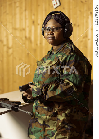 Portrait of army soldier in uniform doing training in shooting range, learning to use pistol. African american woman in firing range practicing with military weapons, wearing protective equipment 123808156