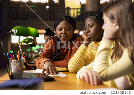 Female teacher assisting pupils with class homework and mentoring them, providing academic instruction and support to help them pass their school assignments. Tutor lecturer gives private lessons. 123808168