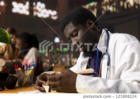 African american medical student learning for a residency exam, studying in the medical academy library, consulting the medical books and scientific studies. Man fighting for a career in medicine. African american medical student learning for a residency exam, studying in the medical academy library, consulting the medical books and scientific studies. Man fighting for a career in medicine. 123808224