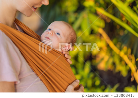 A loving mother walks through a peaceful park, carrying her baby securely in a sling. A heartwarming moment of maternal bonding, babywearing, and the joy of motherhood in nature A loving mother walks through a peaceful park, carrying her baby securely in a sling. A heartwarming moment of maternal bonding, babywearing, and the joy of motherhood in nature 123808413