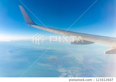 View from the airplane window at a beautiful blue clear sky, earth, sea and the airplane wing View from the airplane window at a beautiful blue clear sky, earth, sea and the airplane wing 123812687