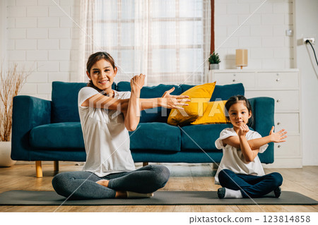 A mother and her daughter create a harmonious family moment at the gym as they engage in stretching and yoga promoting togetherness strength and joyful learning with both wearing smiles of happiness. A mother and her daughter create a harmonious family moment at the gym as they engage in stretching and yoga promoting togetherness strength and joyful learning with both wearing smiles of happiness. 123814858