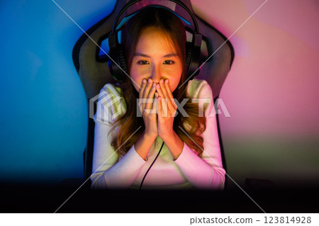 Asian happy Gamer endeavor plays online video games tournament with computer neon light, Smile young woman wearing gaming headphones intend to do playing live stream games online at home, font view 123814928