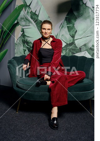 Woman seated on green sofa wearing red outfit in stylish interior setting Woman seated on green sofa wearing red outfit in stylish interior setting 123817734