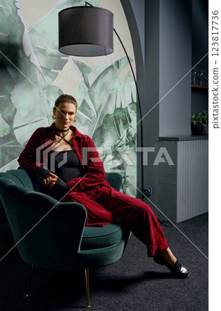 Low key relaxed portrait of a woman in a chair posing in a stylish setting with green decor 123817736