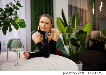 Elegant woman relaxing at a stylish table in a modern indoor setting with green plants 123817753