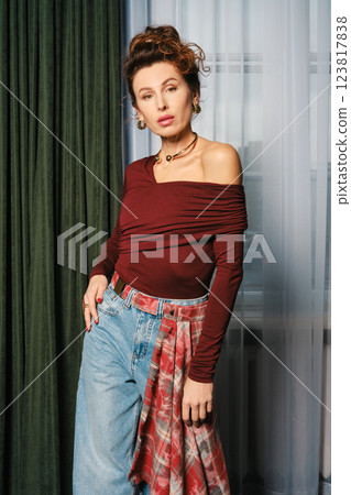 Lifestyle portrait of woman in maroon off-shoulder top and jeans, with a stylish plaid detail 123817838