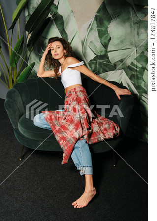 Adult woman lounging gracefully on a velvet sofa against a leafy backdrop 123817842