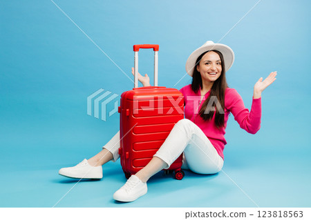 Happy young tourist woman sitting at the suitcase, hugging it and going to travel on holidays isolated on blue background. Happy young tourist woman sitting at the suitcase, hugging it and going to travel on holidays isolated on blue background. 123818563