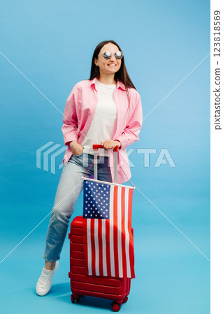 Female tourist with travel suitcase and USA flag, standing isolated on blue studio background 123818569