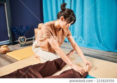 Masseuse making thai yoga massage. Woman therapist doing traditional massage treatment for female patient indoors. Client lying on mat, meditating, enjoying hand massage in calm atmosphere. 123820350