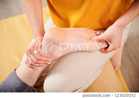 Masseuse making thai yoga massage. Woman therapist doing traditional massage treatment for male patient's foot. Close up. Client lying on mat, meditating, enjoying hand massage in calm atmosphere. 123820352