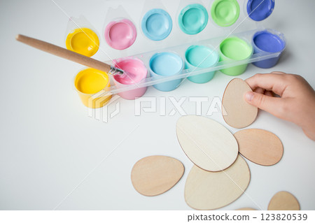 Child painting Easter wooden eggs with colorful acrylic paints and brush 123820539