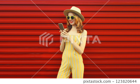 Beautiful happy young woman smiles with mobile phone looking at smartphone on red background 123820644