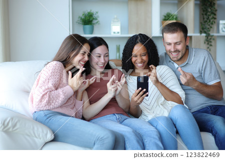 Hopeful happy interracial friends crossing fingers checking phone Hopeful happy interracial friends crossing fingers checking phone 123822469