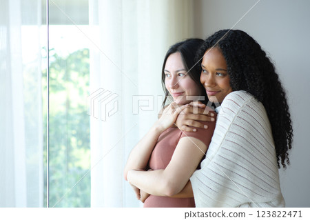Satisfied lesbian interracial couple at home contemplating 123822471