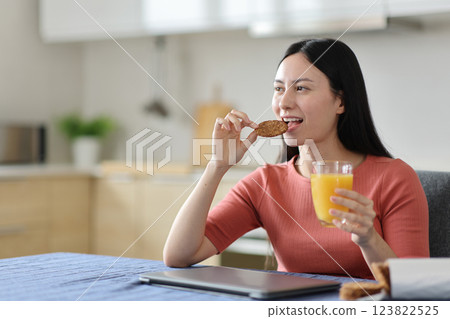 Happy asian woman at breakfast eating cookie drinking orange juice 123822525