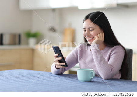 Happy asian woman checking phone content in a kitchen Happy asian woman checking phone content in a kitchen 123822526